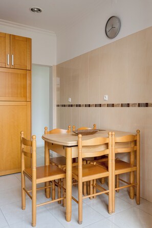 A dining area with a round wooden table and chairs, a clock on the wall, and a wooden cabinet. - Graça Secret Village – 2BR Retreat (Lisbon)