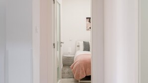 A hallway leading to a bedroom with a bed, a bedside table, and a wall-mounted picture. - Graça Secret Village – 2BR Retreat (Lisbon)