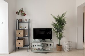 Un salon avec un meuble TV en verre, une plante en pot et une étagère avec des boîtes de rangement.