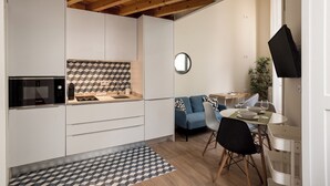 Een moderne keuken met witte kasten, een magnetron en een geometrisch patroon op de achterwand. Er is een zithoek met een blauwe bank en een tafel gedekt voor twee personen.