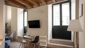 Een moderne woonkamer met een eetgedeelte, een aan de muur bevestigde televisie en een raam met uitzicht op gebouwen.