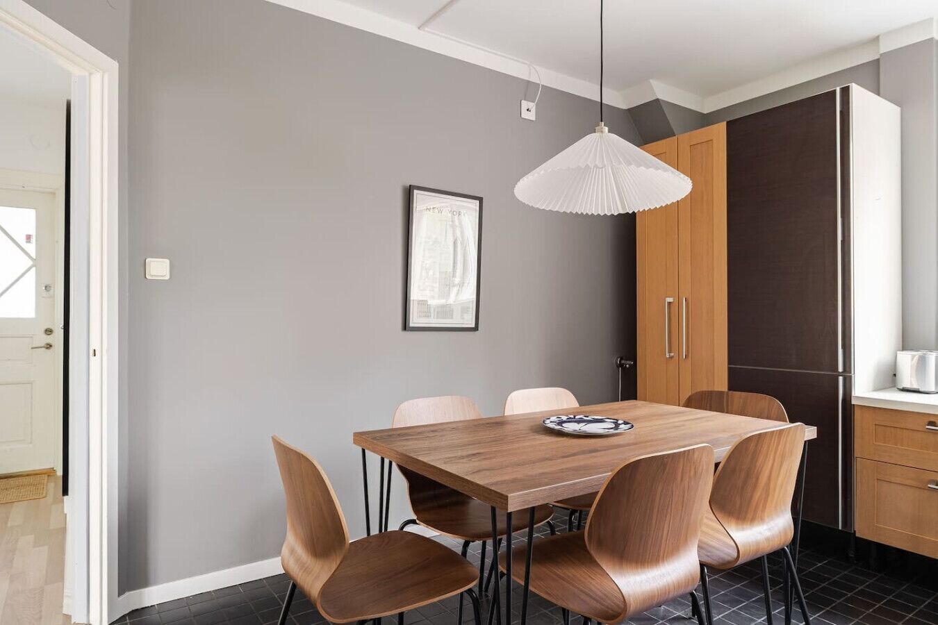 Een moderne keuken met een eettafel, stoelen, een hanglamp en een lijst met een afbeelding aan de muur.