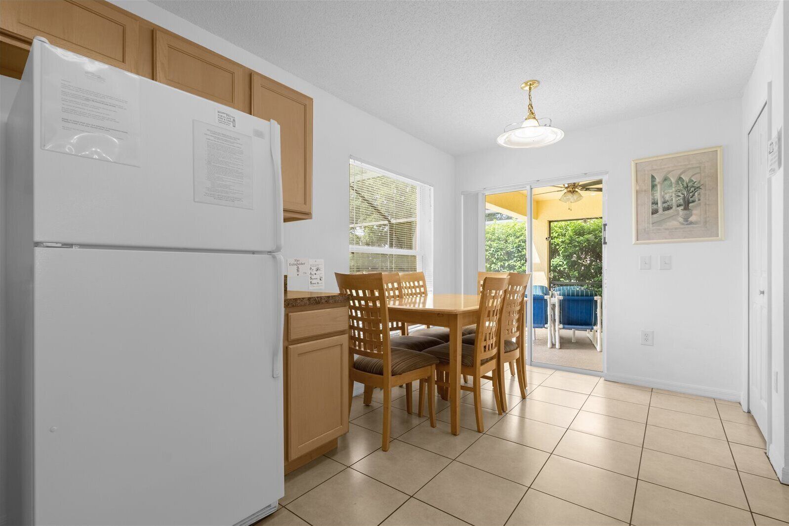 A kitchen with a refrigerator, wooden cabinets, a dining table with chairs, and a ceiling fan.