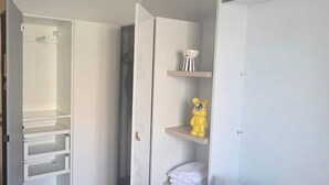 Een slaapkamer met een bed, een kledingkast, een plank met een teddybeer, en een spiegel.