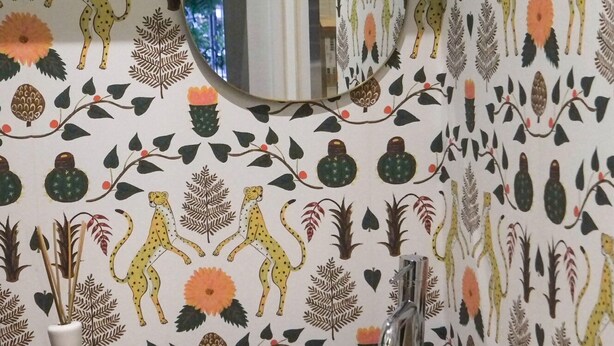 Een badkamer met een ronde spiegel, een beige wastafel en behang met dieren en planten.