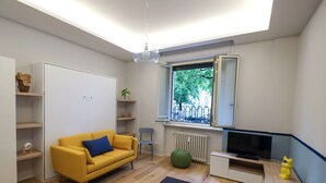 Een moderne woonkamer met een bank, televisie en een raam met uitzicht op bomen.