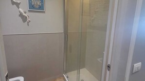 Een badkamer met een douchecabine van glas, een toilet en een beige vloerkleed.