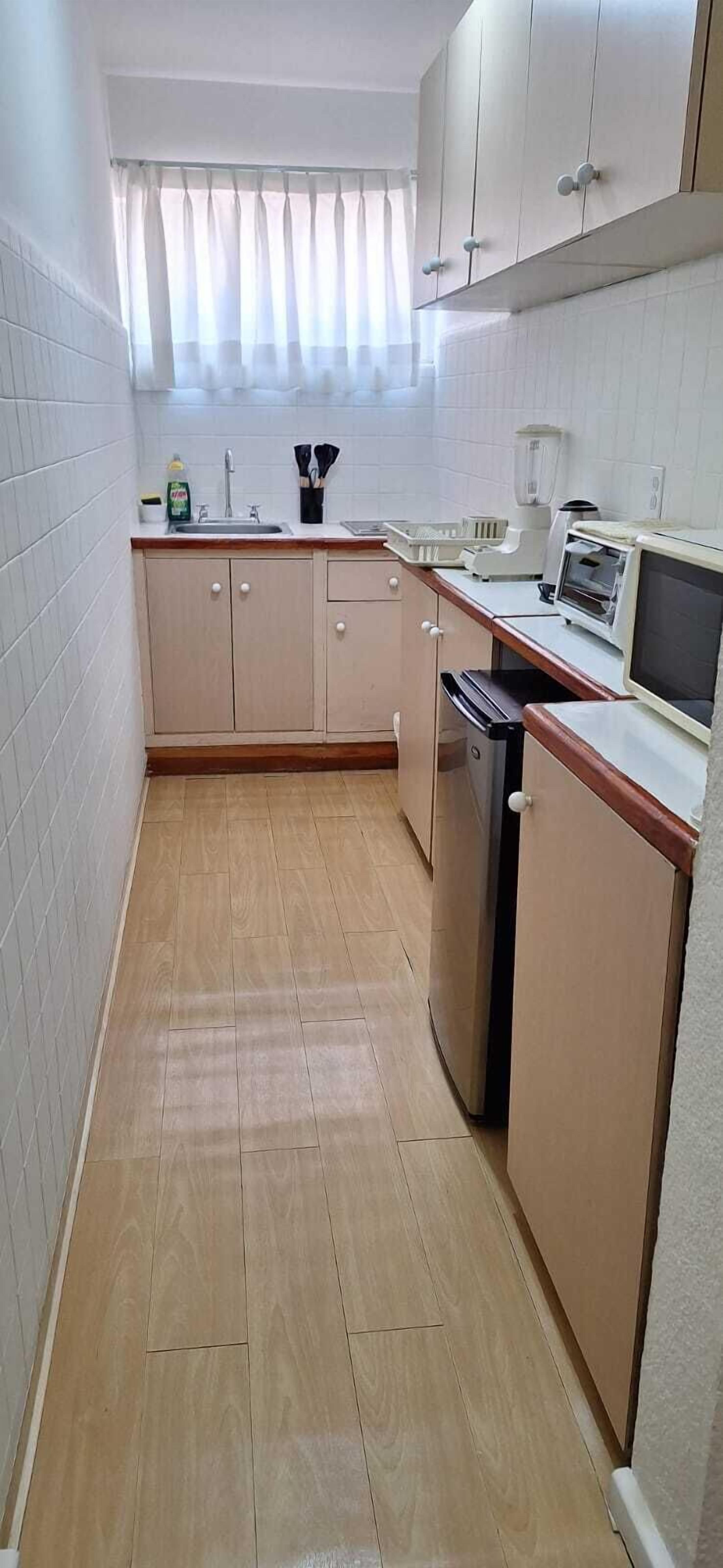 A compact kitchen with white cabinets, a wooden countertop, a dishwasher, and a microwave.