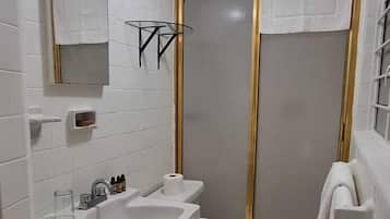 Baño con lavamanos, inodoro y zona de ducha blanca.