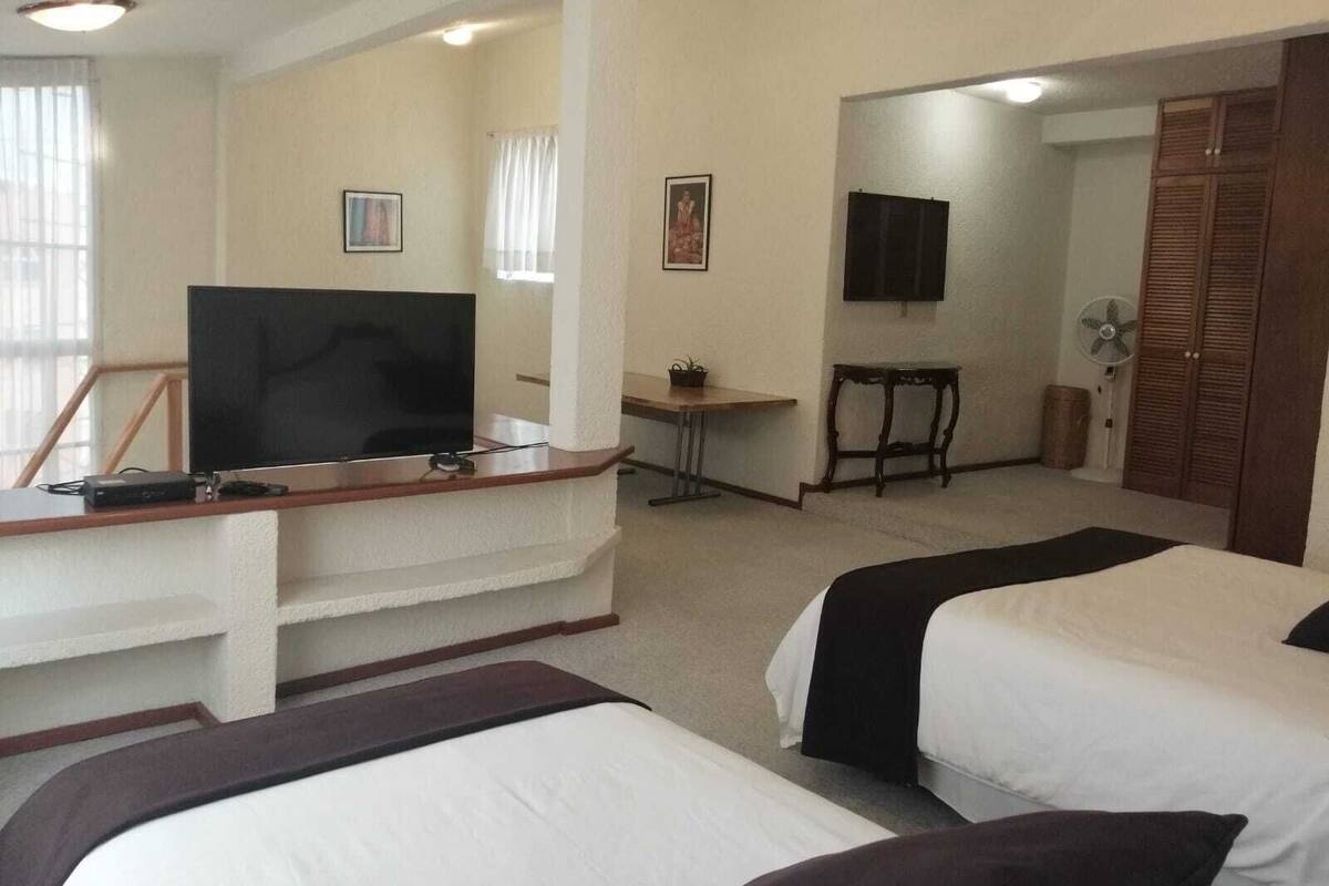 A hotel room with two beds, a desk with a TV, a small table, and a wardrobe.