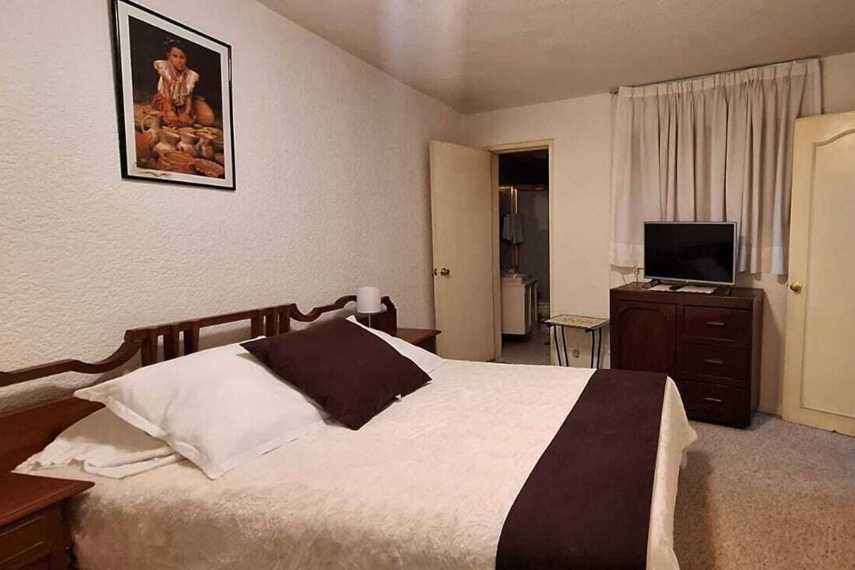 A bedroom with a bed, a dresser, a television, and a door.
