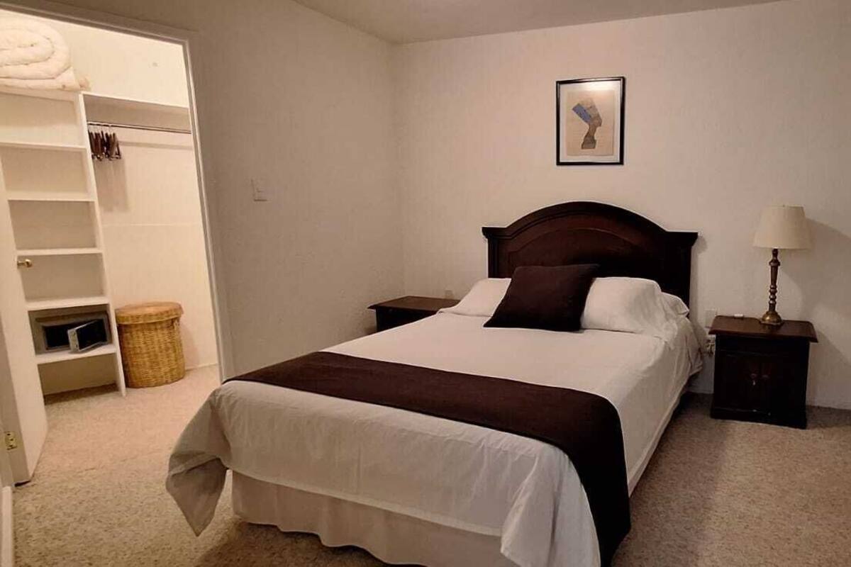 A neatly arranged bedroom with a bed, bedside tables, a lamp, a wardrobe, and a framed picture on the wall.