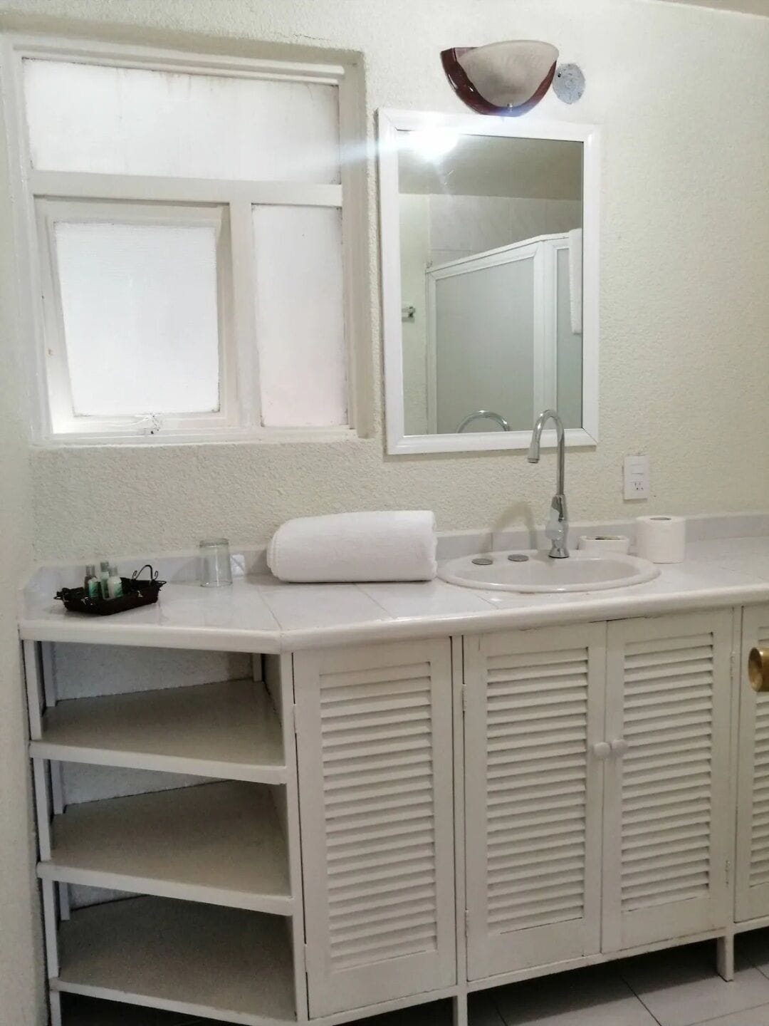 A bathroom with a white sink, mirror, and a shelf with toiletries.