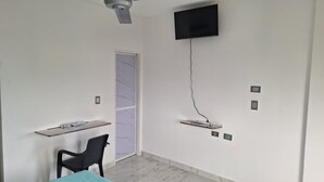 A room with a ceiling fan, a TV mounted on the wall, a chair, a table, and a door with a view.