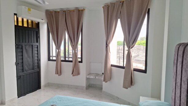A room with a bed, a window with curtains, a door, and a small table.