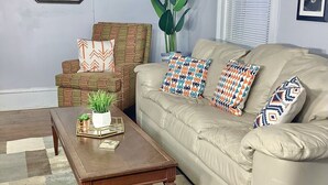 Een woonkamer met een bank, fauteuil, bijzettafeltje en een grote plant.