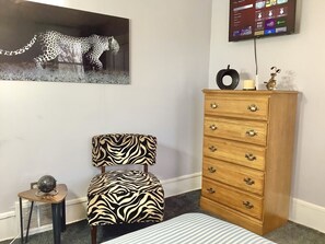 A bedroom with a zebra-patterned chair, a wooden dresser, a globe on a small table, and a TV mounted on the wall. - Near downtown, Ohio City, Walkable, Flats! (Cleveland)