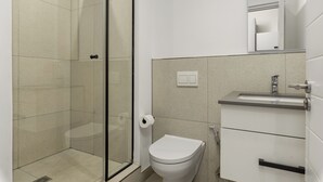 Et stilfuldt badeværelse med glasvæg omkring bruseren, toilet, vask og spejl.