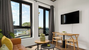 En moderne stue med sofa, et rundt bord, fjernsyn ophængt på væggen og udsigt gennem store vinduer.