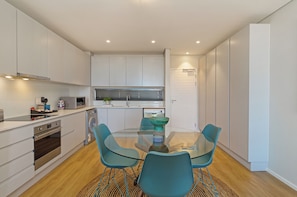 A modern kitchen with white cabinetry, a glass dining table, and teal chairs. - Mountain View Luxe | Modern Century City Stay (Cape Town)
