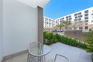 En balkon med et glasbord og stole, flisegulv og udsigt til en bygning med flere vinduer.