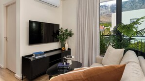 Un salon moderne doté d’un téléviseur à écran plat, d’une table basse noire, d’un canapé, d’une plante en pot et offrant une vue sur un paysage montagneux grâce à de grandes fenêtres.