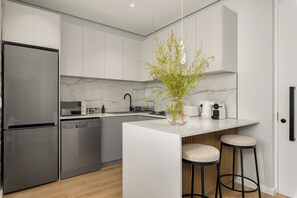 A modern kitchen with a built-in refrigerator, dishwasher, and a marble countertop island with stools. - Modern 1 Bedroom Apartment in Green Point (Cape Town)
