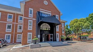 A brick building with a black awning labeled 'BLOCK 2,' large windows, and a paved entrance area. - Chic 2BR in Illovo: Work, Play, Unwind (Johannesburg)