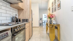 A modern kitchen with a gas stove, oven, and a dining area with a chair and table. - Chic 2BR in Illovo: Work, Play, Unwind (Johannesburg)