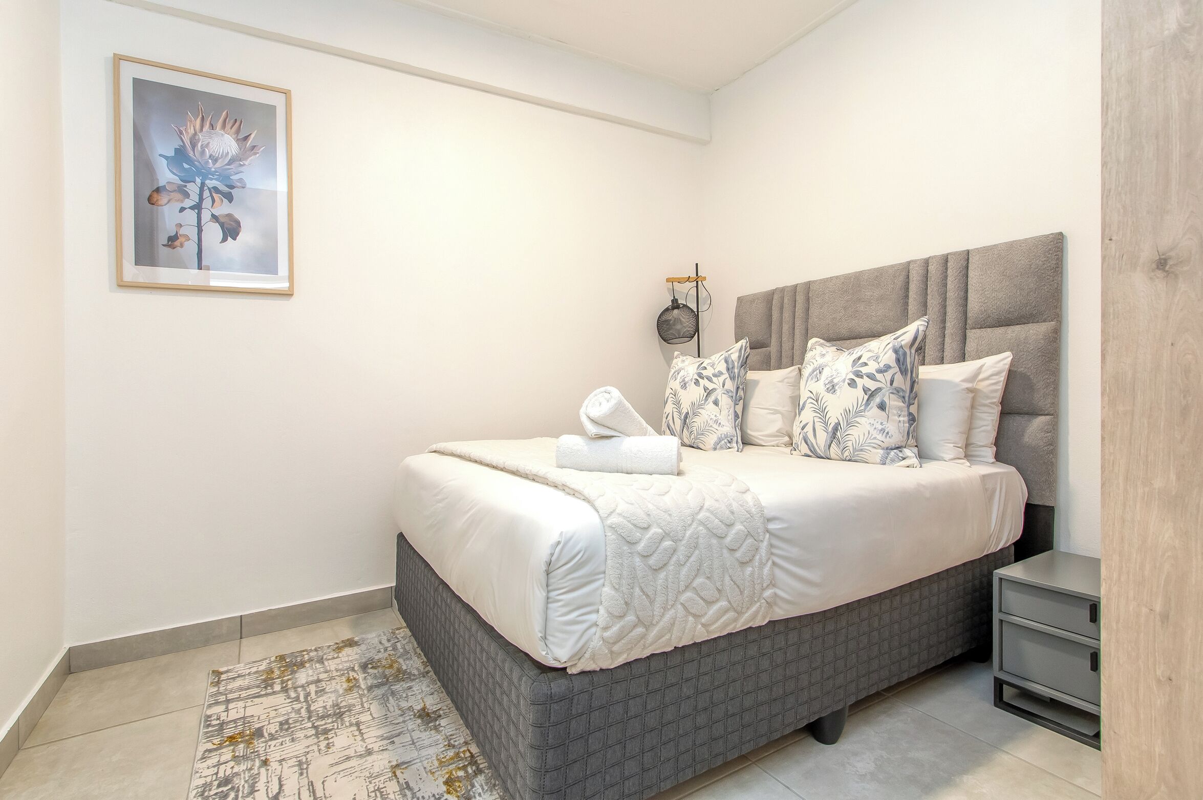 A neatly made bed with a headboard, a bedside table, and a framed picture on the wall.