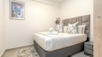 A neatly made bed with a headboard, a bedside table, and a framed picture on the wall.