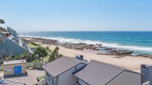 A coastal view with a rocky beach, a clear sky, and residential buildings.