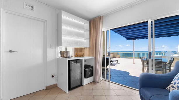 A compact kitchen with a refrigerator, a sink, and a countertop. There is a sliding glass door leading to a balcony with outdoor furniture.