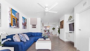 A modern living room with a blue sofa, white coffee table, and artwork on the walls.