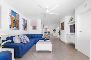 A modern living room with a blue sofa, white coffee table, and artwork on the walls. - Luxury Penthouse in Ballito | Beach and Pool Access (Dolphin Coast)