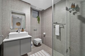 A modern bathroom with a glass shower enclosure, a white sink with a mirror, and a small toilet.