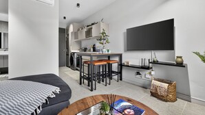 A modern living room with a sofa, a coffee table, a kitchen area with stools, and a mounted TV. - Stylish 2 Bedroom | Zimbali | Pool and Braai (Dolphin Coast)