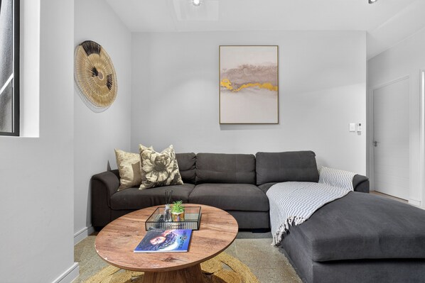 A modern living room with a dark grey sofa, a round wooden coffee table, and a large abstract painting on the wall.