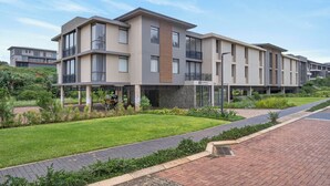 A modern multi-story residential building with balconies, a landscaped garden, and a paved walkway. - Stylish 2 Bedroom | Zimbali | Pool and Braai (Dolphin Coast)