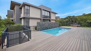 A modern two-story house with a swimming pool, a stone wall, and a wooden deck. - Stylish 2 Bedroom | Zimbali | Pool and Braai (Dolphin Coast)