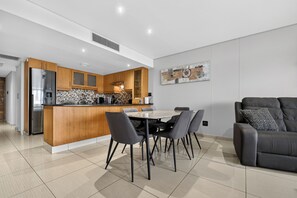 A modern kitchen with a central island, dining table with chairs, and a grey sofa. - Palm Boulevard 404 | 3Bed Luxury - Gateway (Umhlanga)