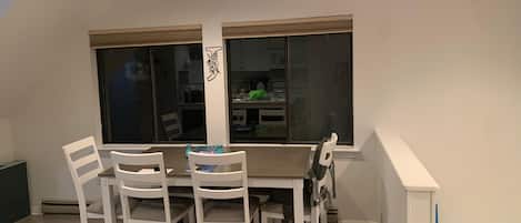 Ein Essbereich mit einem Tisch, vier Stühlen, einem Fenster mit Jalousien und einer Deckenleuchte.