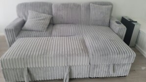 Um sofá cinza estofado com um banquinho a combinar e uma mesinha de apoio num quarto com radiador e mala.