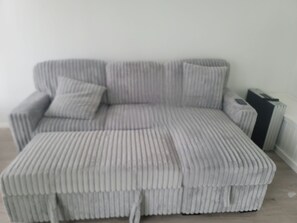 Un sofá tapizado gris con un reposapiés a juego y una mesita de noche en una habitación con un radiador y una maleta.