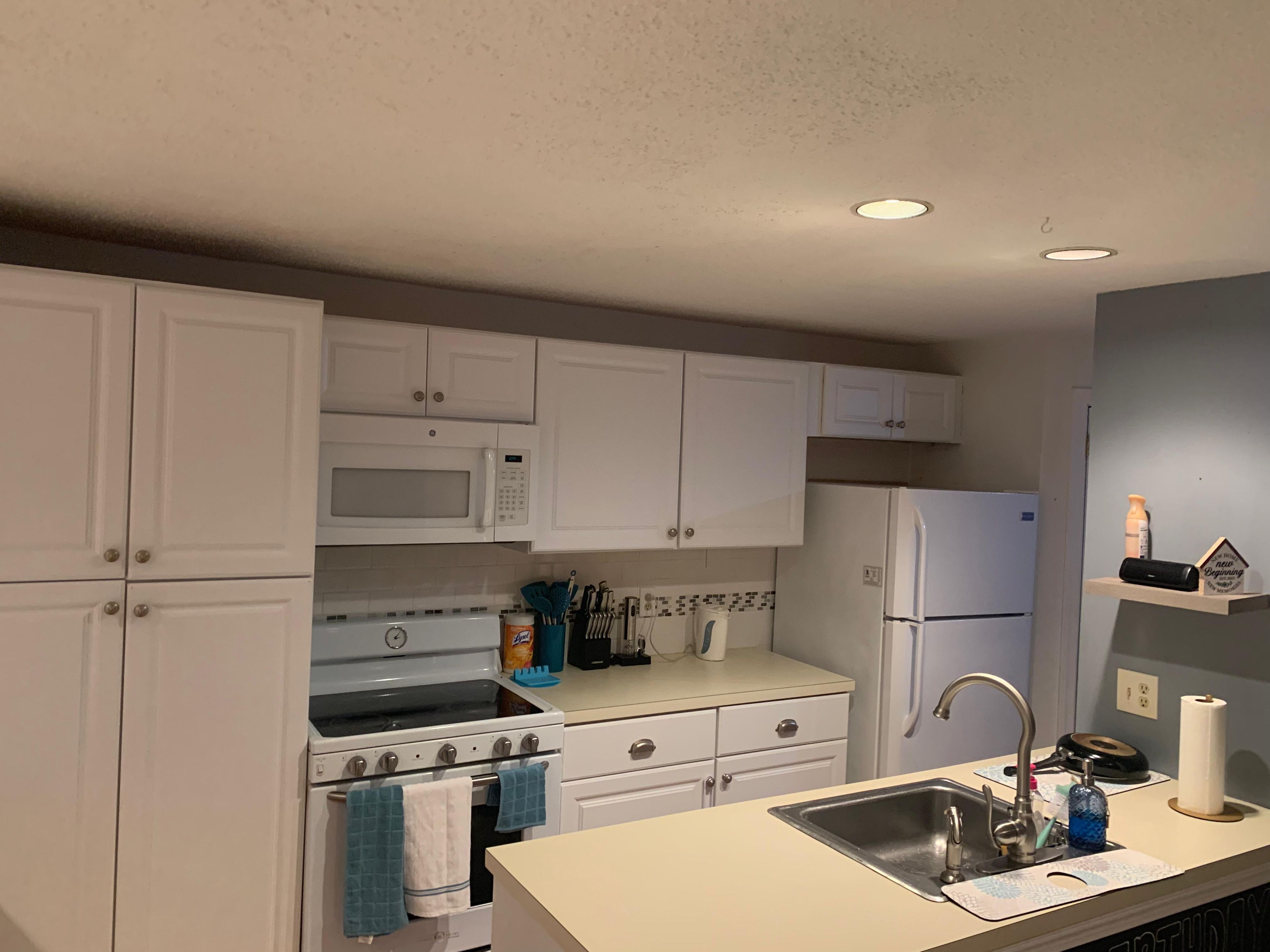 A kitchen with white cabinets, a microwave, a stove, a refrigerator, and a sink.