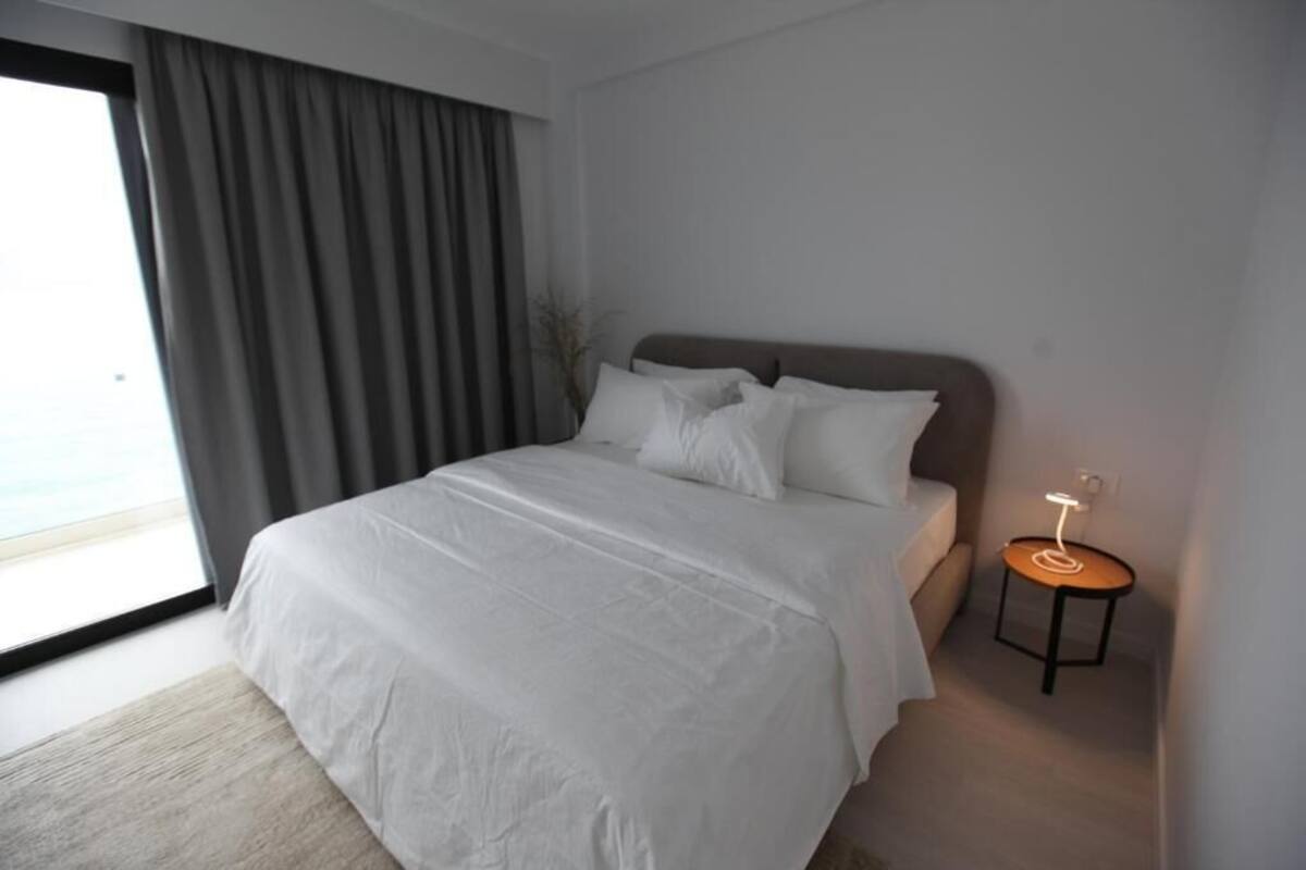 Une chambre d’hôtel moderne, dotée d’un grand lit, d’une table de chevet avec une lampe et offrant une vue sur l’extérieur par une fenêtre.