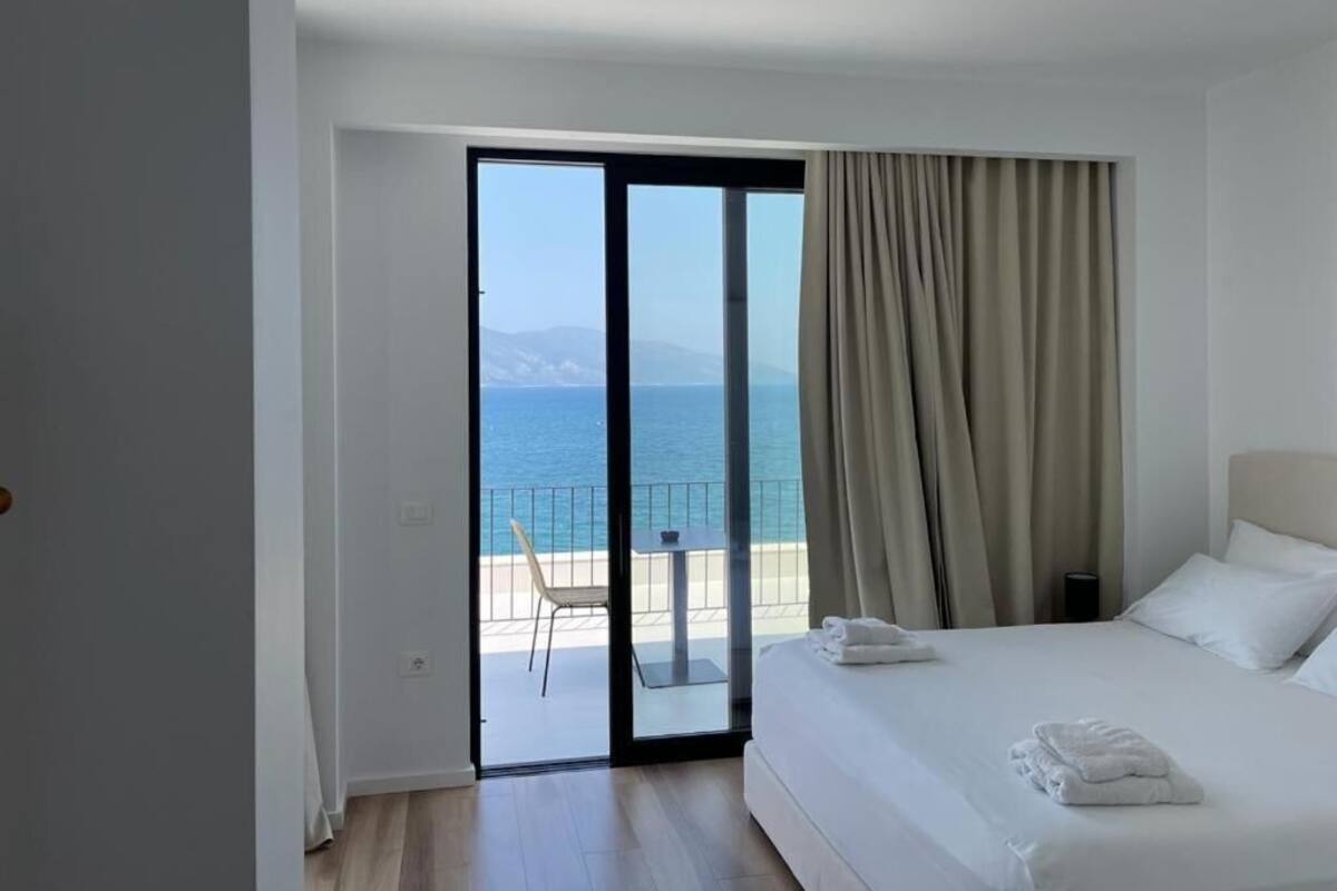 Une chambre d’hôtel avec un lit, une vue sur la mer et un balcon équipé d’une table et de chaises.