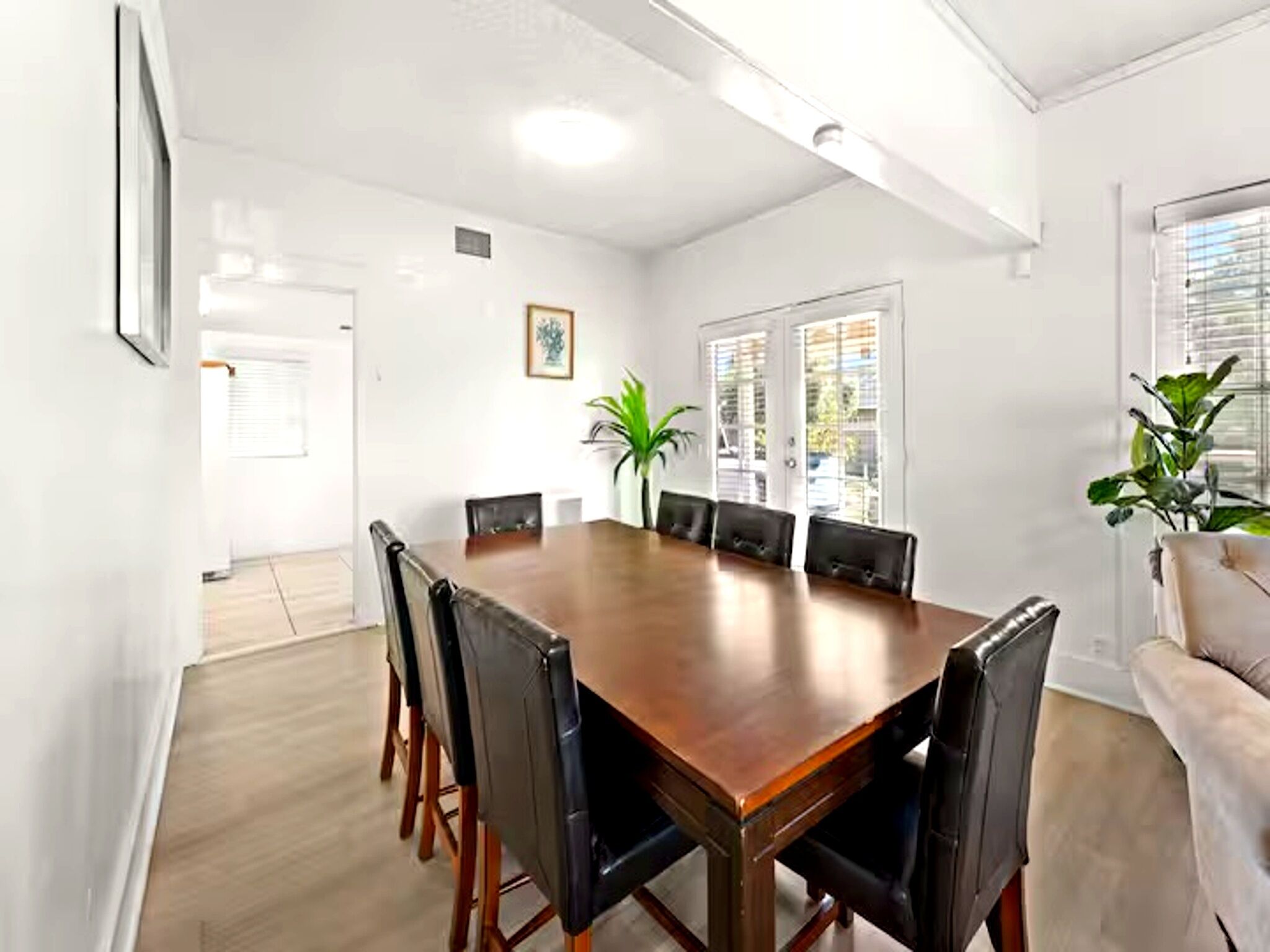 Une salle de conférence avec une table en bois et des chaises noires, des murs blancs et une plante en pot.