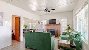 A spacious living room with a green sofa, a fireplace, and a television mounted above it. - Guest Favorite Spacious Home w/ huge Yard, Sleeps 15, Near Dining & Attractions (Rialto)