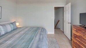 Une chambre à coucher avec un lit, un téléviseur, une commode en bois et un ventilateur de plafond.